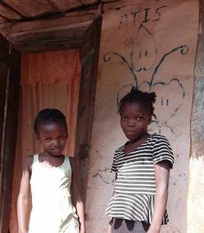 Two young Haitian girls standing by a wooden door