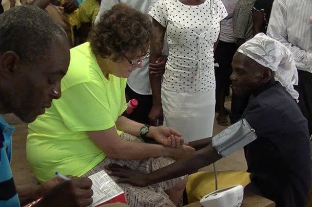 A volunteer in a bright green shirt takes a patient's blood pressure at a community clinic while others look on